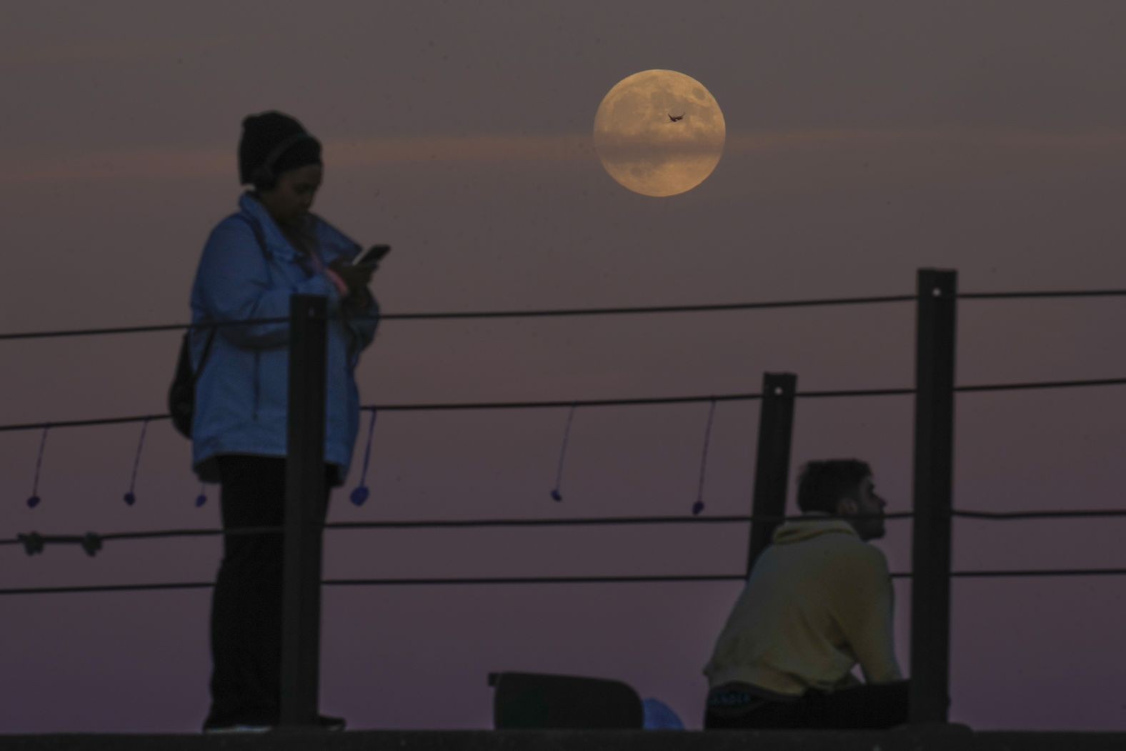 An airplane crosses the supermoon as people watch it rise over Lake Michigan in Chicago.